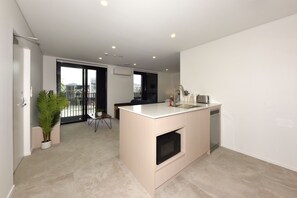 A modern kitchen with a central island, a built-in oven, and a dishwasher. - Christchurch City Studio With Private Balcony (Christchurch)