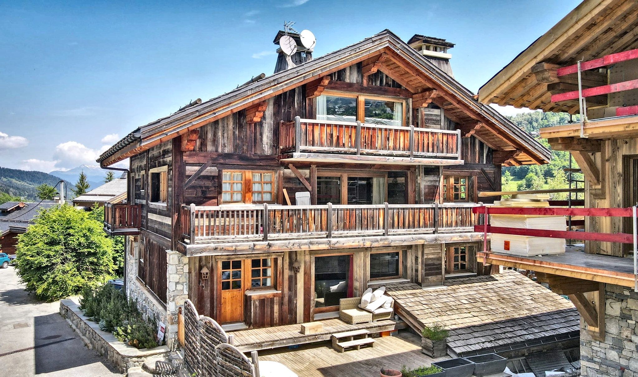 A multi-story wooden chalet with balconies, large windows, and a stone foundation.