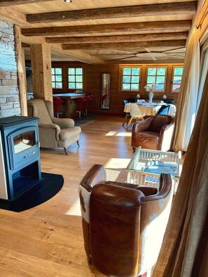 Ein gemütliches Blockhaus-Interieur mit Steinwand, Holzbalken, Kamin, Ledersesseln und einem Essbereich.