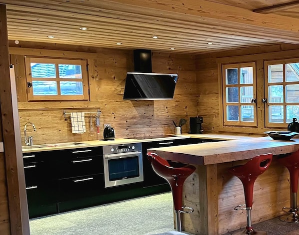 Eine Küche mit Holzwänden, einer schwarzen Dunstabzugshaube, einem Edelstahlbackofen und einer Bar mit roten Barhocker.