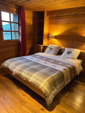 Ein Zimmer mit Holzboden, einem Bett, einem Fenster und einer Lampe.