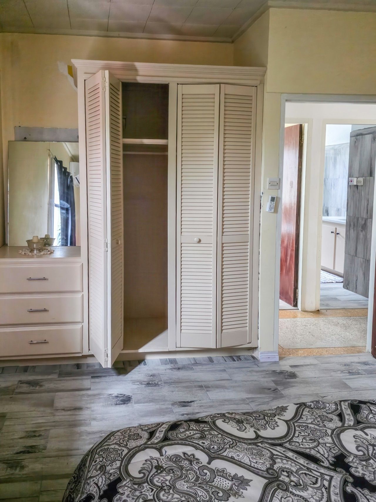 A bedroom with a wardrobe, a dresser, and a patterned bedspread.