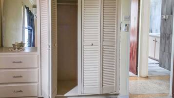 A bedroom with a wardrobe, a dresser, and a patterned bedspread.
