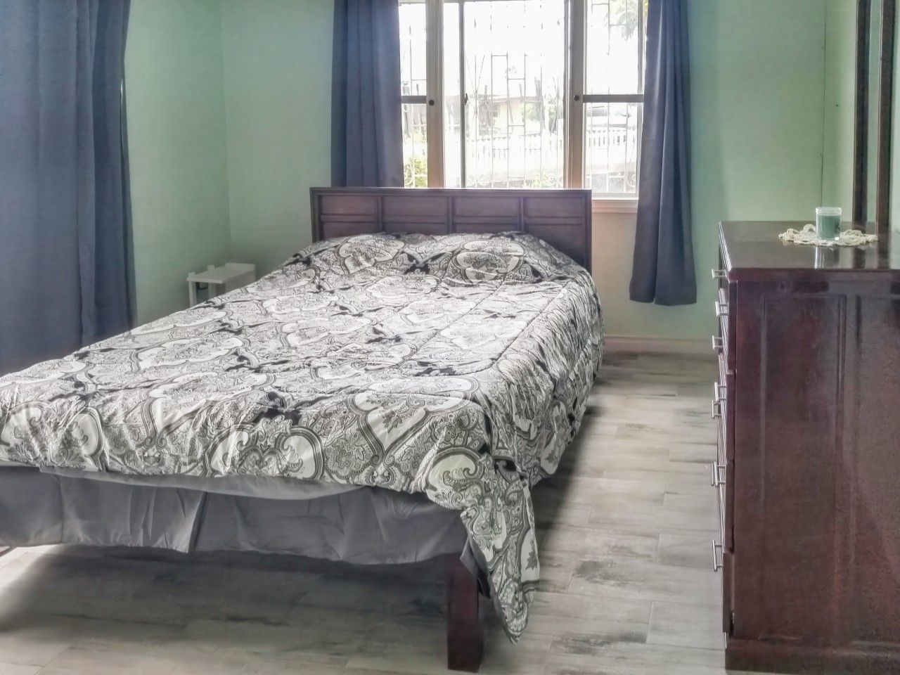 Une chambre à coucher avec un lit, une table de chevet, une commode et une fenêtre avec des rideaux.