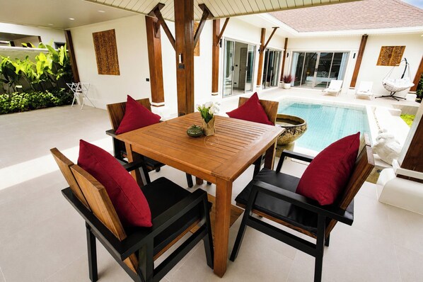 A wooden table with chairs, a pool, and a view of the house.