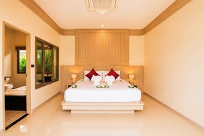 A hotel room with a large bed, bedside lamps, a wooden headboard, and a view of greenery outside.