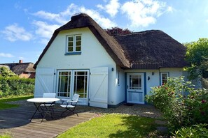 A thatched-roof house with a white exterior, a wooden deck, and a garden with flowers. - Holiday home in Wyk on Föhr with terrace (Wyk auf Föhr)