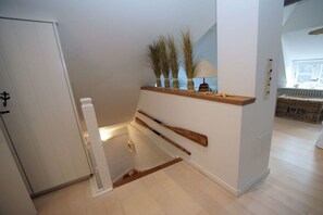 A hallway with a wooden bench, a wall-mounted shelf with decorative items, and a door with a sign. - Holiday home in Wyk on Föhr with terrace (Wyk auf Föhr)