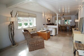 A spacious living area with a sofa, two wicker chairs, a wooden coffee table, and a dining table with chairs. There are windows with curtains, a lamp, and a wall-mounted mirror. - Holiday home in Wyk on Föhr with terrace (Wyk auf Föhr)
