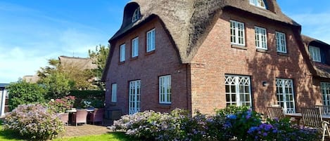 A large brick house with a distinctive thatched roof and multiple windows.