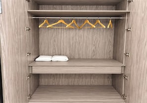 A wooden wardrobe with two shelves, one holding a pair of white towels and the other empty. - Stavora Suites (Gurugram)