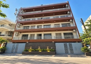 A multi-story building with balconies, a gated entrance, and a landscaped area with plants. - Stavora Suites (Gurugram)