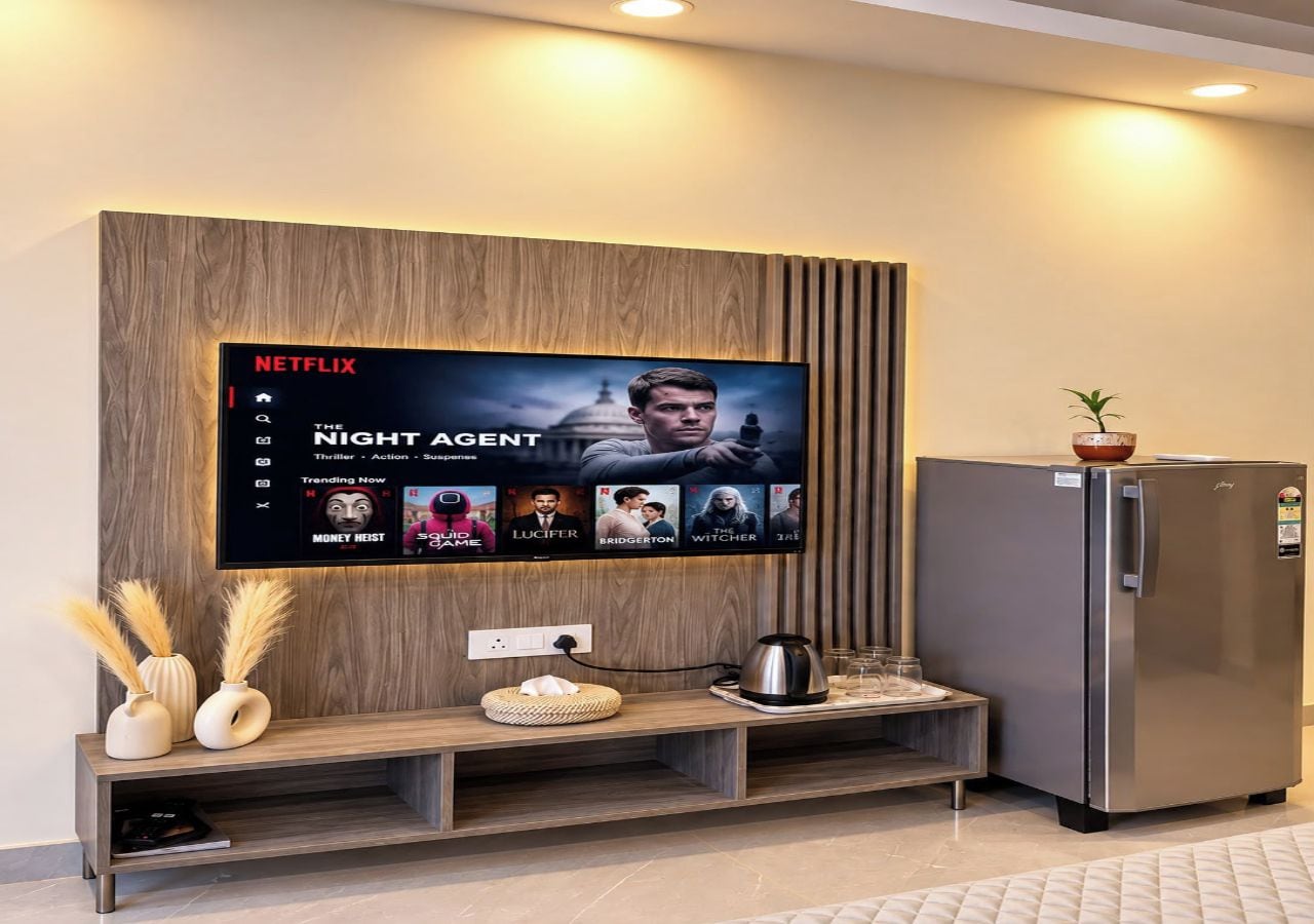A modern living area with a mounted television displaying a Netflix interface, a built-in refrigerator, and a wooden accent wall.