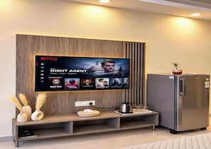 Un espacio de sala moderno con un televisor de pared mostrando la interfaz de Netflix, un refrigerador empotrado y un revestimiento de pared de madera.