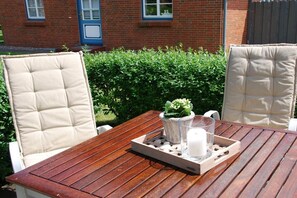 A wooden table with a tray, two cushioned chairs, a potted plant, and a candle. - Holiday apartment in Wrixum with terrace (Wrixum)