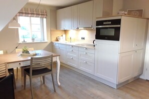 A kitchen with white cabinets, a black oven, a dining table with chairs, and a window with curtains. - Holiday apartment in Wrixum with terrace (Wrixum)