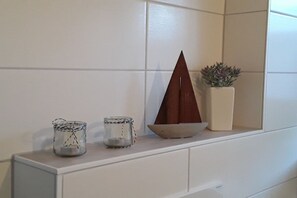 A white tiled wall with a shelf holding a small wooden boat, two glass jars with string, and a potted plant. - Holiday apartment in Wrixum with terrace (Wrixum)