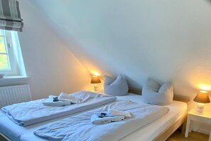 Uma cama de solteiro com roupa de cama e almofadas brancas, duas luminárias de cabeceira e uma janela com cortinas.