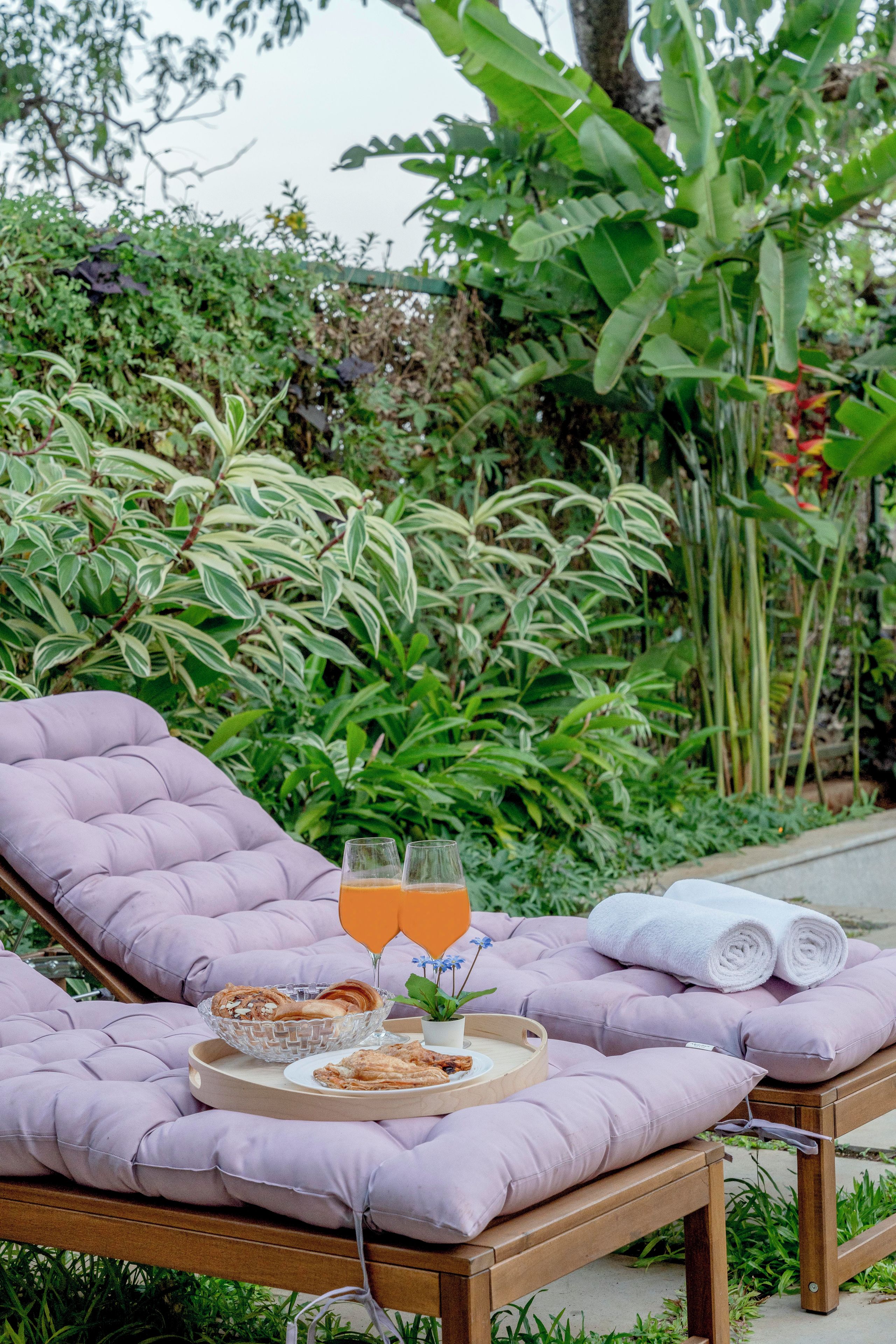A lounge chair with a tray of food and drinks, set against a backdrop of lush greenery.