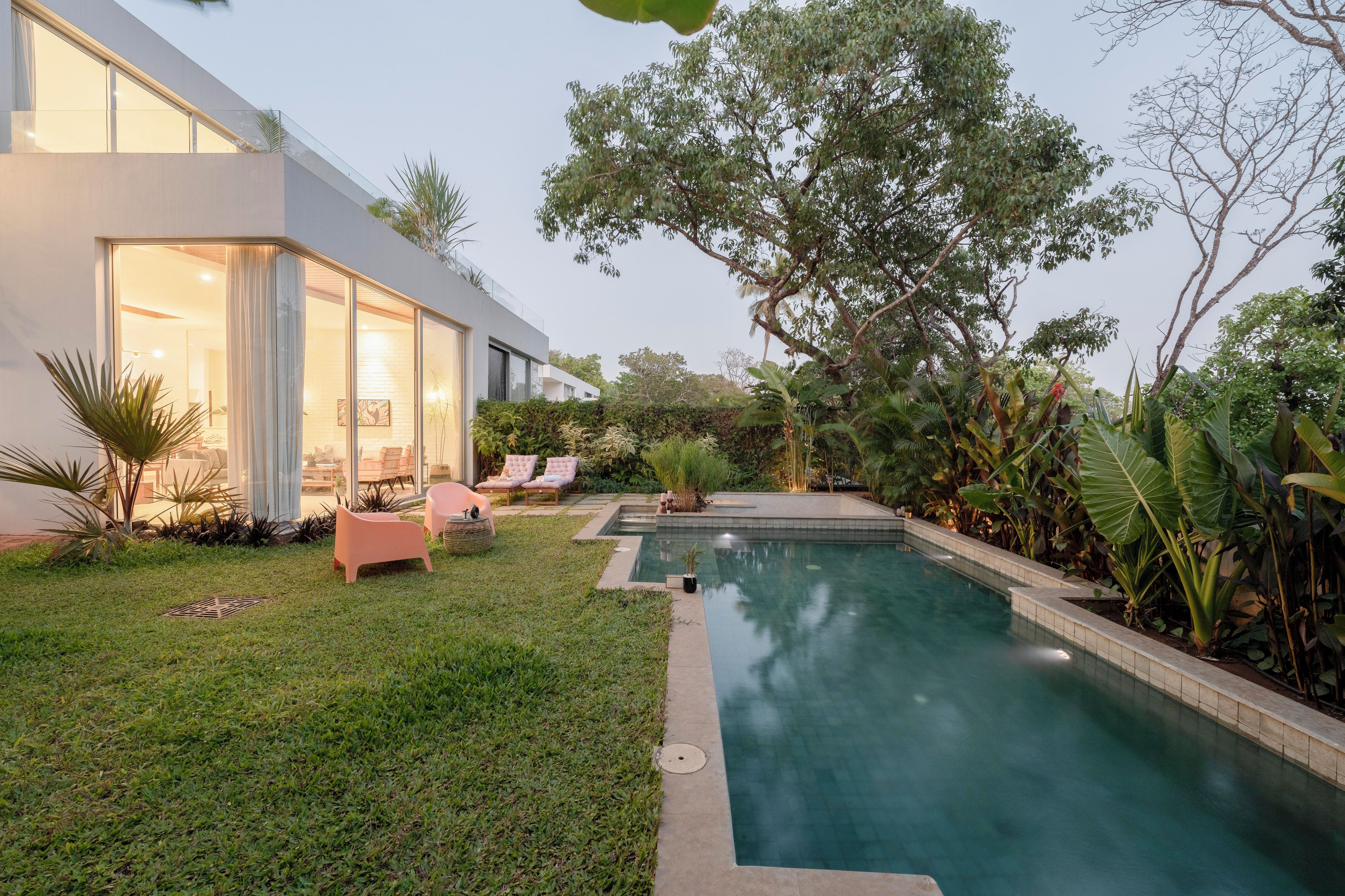 A modern house with a swimming pool, outdoor seating, and lush greenery.