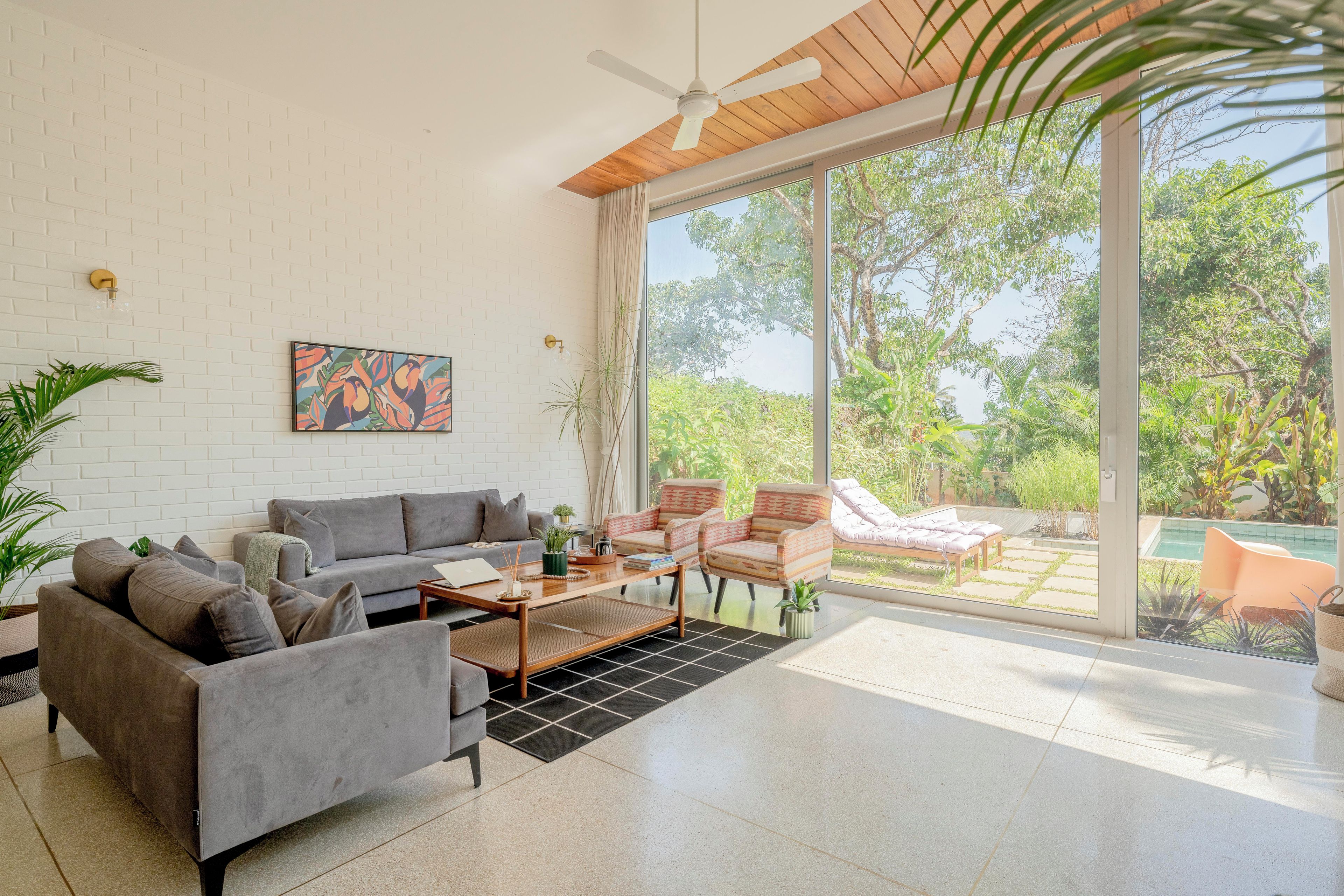 A modern living room with a grey sofa, a coffee table, and a view of a lush garden through large windows.