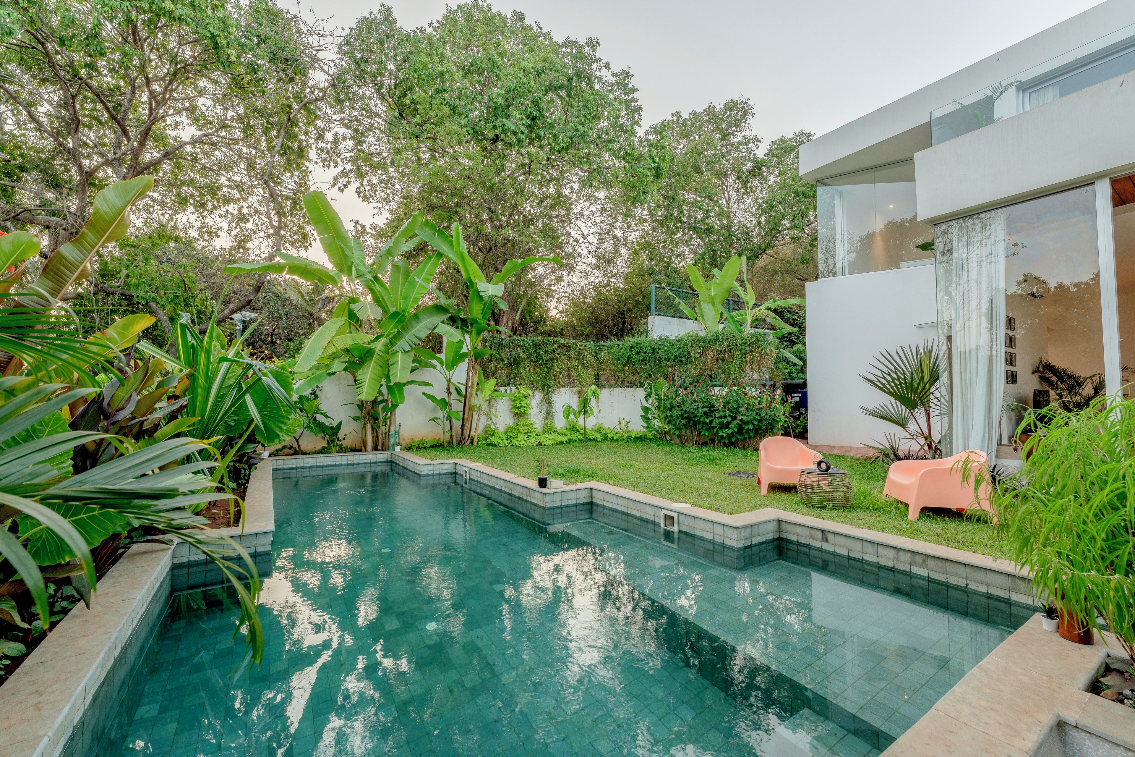 A swimming pool with a tiled edge, surrounded by lush greenery and a modern building with large windows.