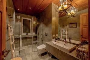 Un baño moderno con cabina de ducha de vidrio, inodoro, tocador grande con lavamanos dobles y techo de madera.