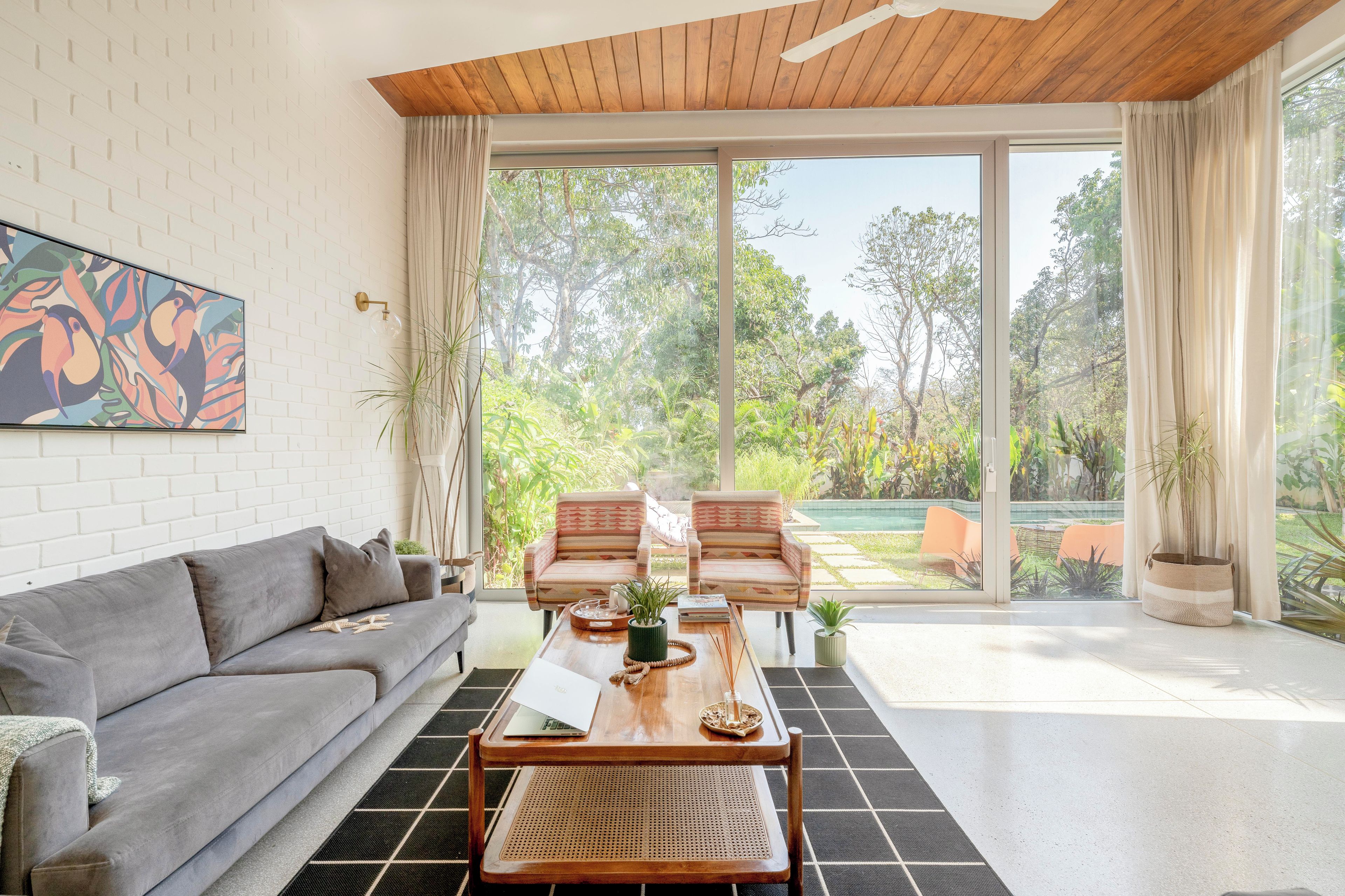 A modern living room with a sofa, chairs, a coffee table, and a large sliding glass door leading to a garden.