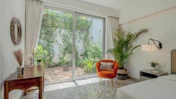 Quarto de hotel com cama, cadeira, mesa, planta em vaso e vista para o verde lá fora.