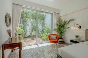 Habitación de hotel con cama, una silla, una mesa, una planta en maceta y vistas al exterior con vegetación.