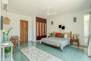 Un dormitorio con una cama, mesitas de noche, una silla, un ventanal grande y un ventilador de techo.