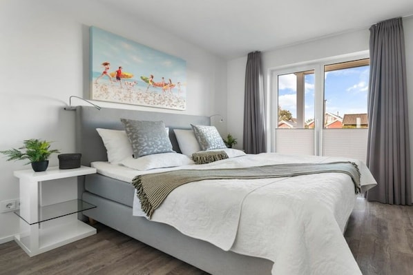 A modern bedroom with a bed, bedside tables, a painting, and a view through the window. - Holiday apartment with 2 bedrooms (Olpenitz)