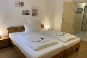 Un lit double avec du linge de lit blanc et des oreillers, une tête de lit en bois, des lampes de chevet et une porte donnant sur une salle de bain.