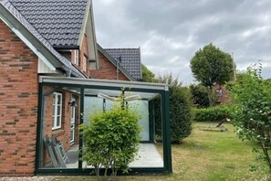 Ein Haus mit Wintergarten, Ziegelaußenwand und Rasen mit Rasenmäher.