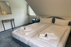 Ein Doppelzimmer mit zwei Betten, einem kleinen Tisch, einem Nachttisch, einem Spiegel und einem Fenster.