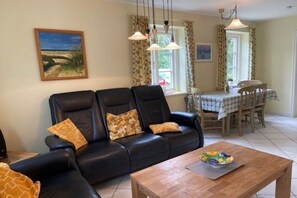 A living room with a black leather sofa, a wooden coffee table, and a dining area with a table and chairs. - Green Eilun House Section 1 (Wyk auf Föhr)
