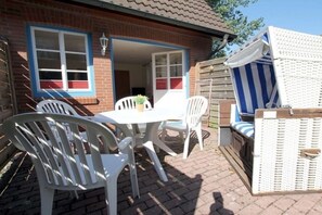 A patio with a table and chairs, a wicker sofa, and a striped chair. - Badestraße 40a - Holiday Apartment 1 (Wyk auf Föhr)