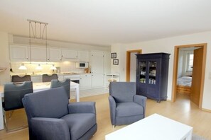 A modern living room with a dining area, a kitchen with white cabinets, and a dark-colored cabinet. - Badestraße 40a - Holiday Apartment 1 (Wyk auf Föhr)