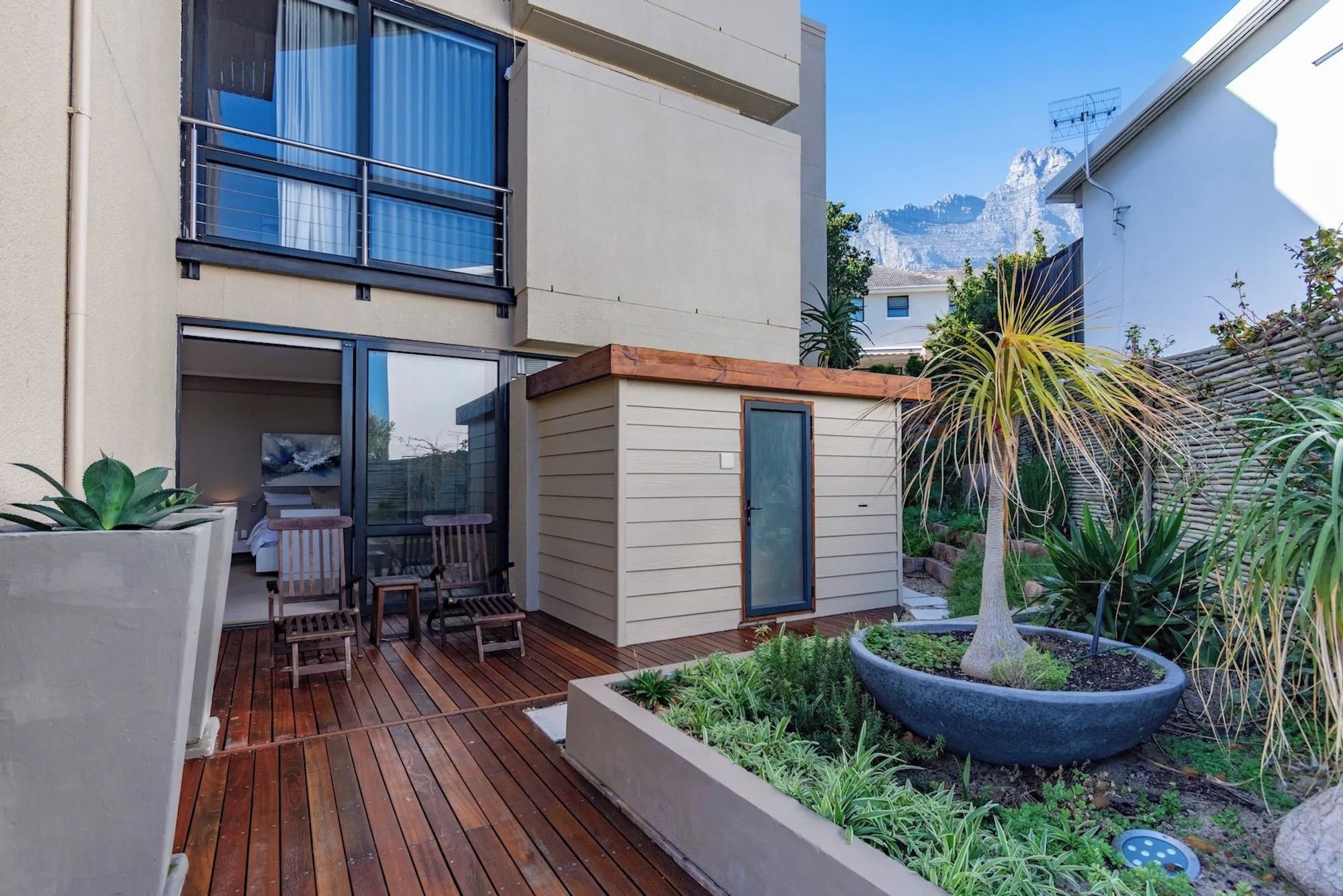 Eine moderne Außenpatio mit Holzboden, einer kleinen Sitzecke und einem Garten mit verschiedenen Pflanzen.