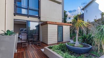 Eine moderne Außenpatio mit Holzboden, einer kleinen Sitzecke und einem Garten mit verschiedenen Pflanzen.