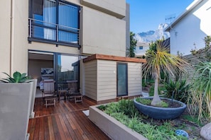 Eine moderne Außenpatio mit Holzboden, einer kleinen Sitzecke und einem Garten mit verschiedenen Pflanzen.