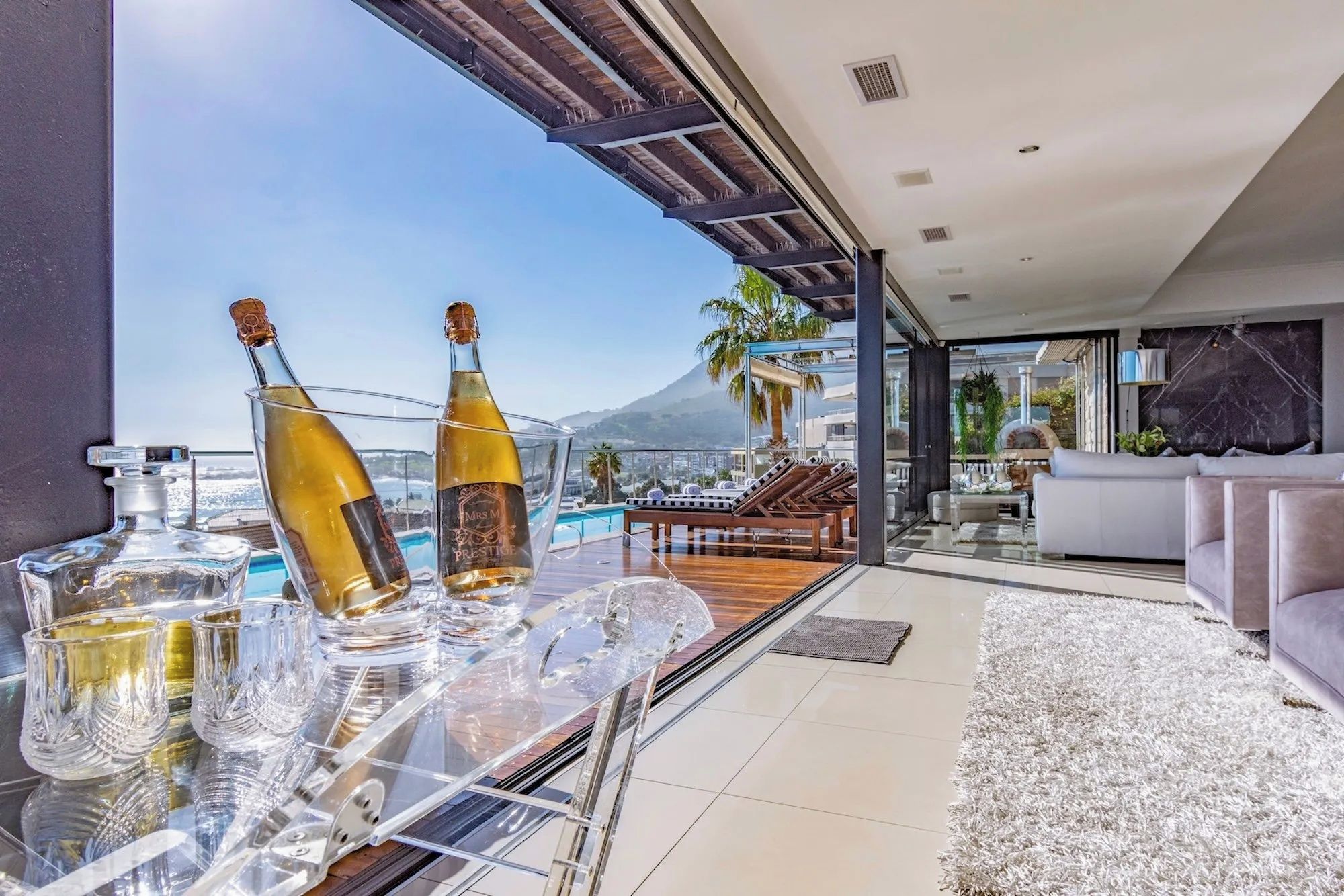 Un salon moderne avec une table en verre, deux bouteilles de champagne et une vue sur une montagne.