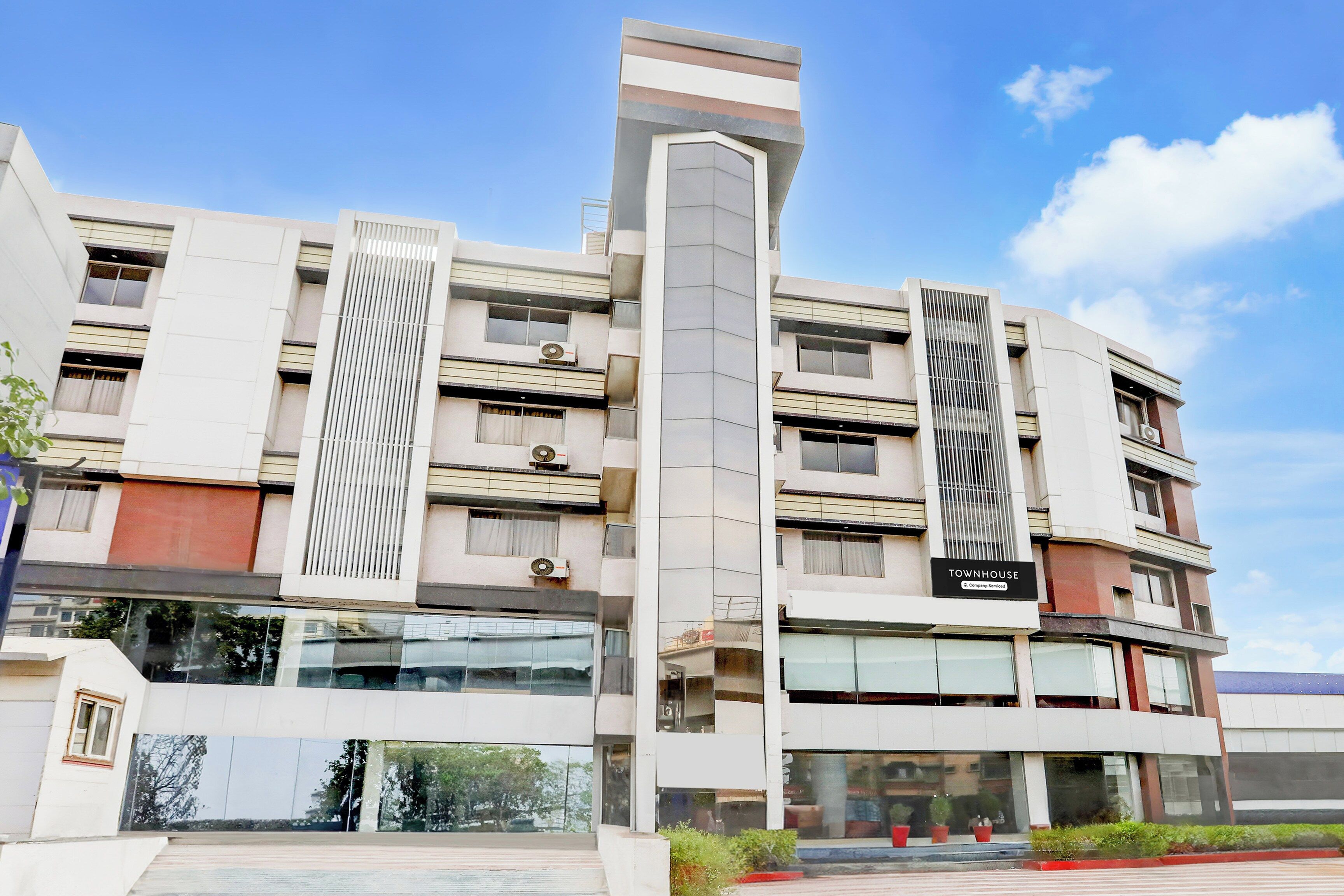 Un edificio de varios pisos con un diseño arquitectónico moderno, que presenta un elemento vertical destacado y un letrero que indica que se trata de una casa townhouse de servicio de la empresa.