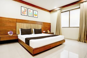 Habitación de hotel con una cama grande, cabecera de madera y una mesita de noche con un florero.