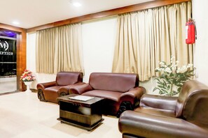 A hotel reception area with leather sofas, a coffee table, and a red fire extinguisher on the wall. - Townhouse Prahladnagar (Ahmedabad)