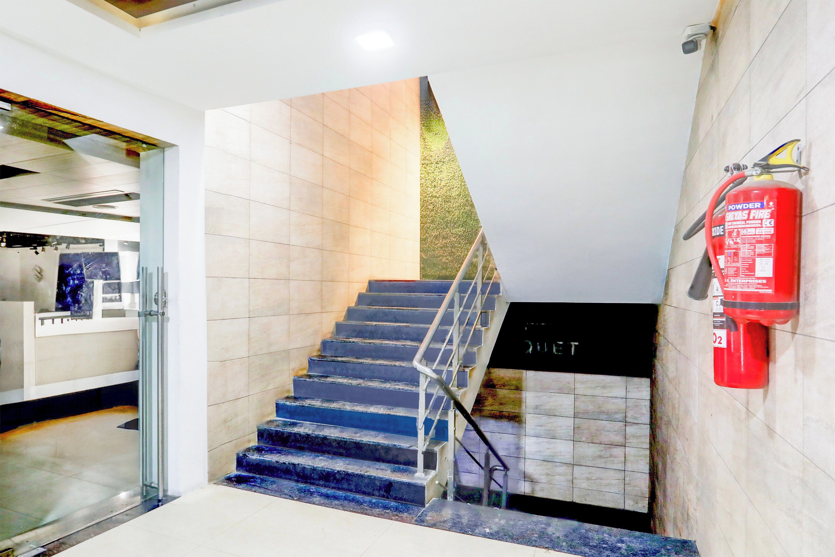 A staircase with a glass railing leading to a landing with a fire extinguisher mounted on the wall.