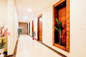 Pasillo de hotel con puertas de madera, plantas en macetas y suelo de baldosas.