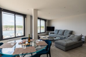 A modern living room with a glass dining table, grey sofa, and a flat-screen TV. - Panoramic Sea-view Apartment in Le Conquet (Le Conquet)