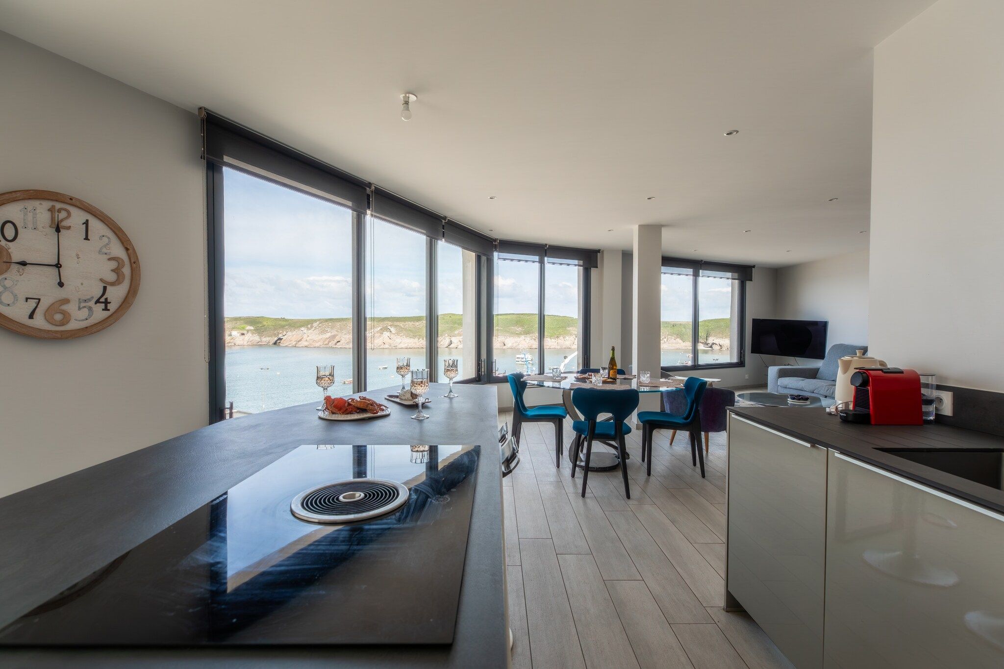 A modern kitchen with a large island, dining area with chairs, and a view of the sea.