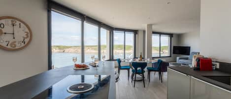 A modern kitchen with a large island, dining area with chairs, and a view of the sea.